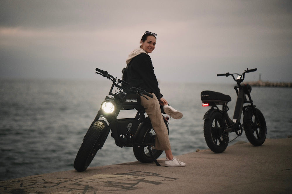 A woman stands with her black ebike by seaside
